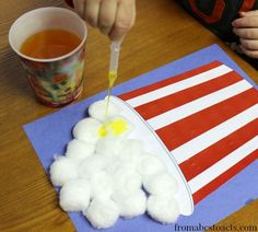 a child is painting an american flag with white cotton balls on a blue piece of paper