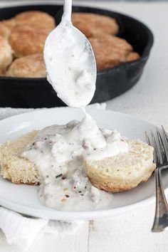 a plate with biscuits and gravy being drizzled over it by a fork