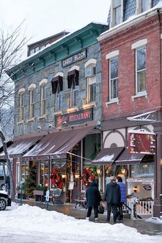 two people are walking down the street in front of a restaurant on a snowy day