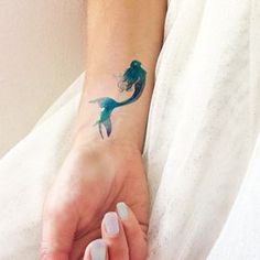 a woman's hand with a small tattoo on her wrist and the shape of a mermaid tail