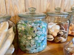 several glass jars filled with different types of seashells on a wooden counter top