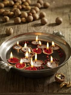 a metal pan filled with lots of candles on top of a wooden table next to nuts