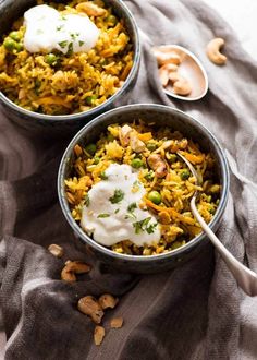 two bowls filled with rice, peas and cashews on top of a table