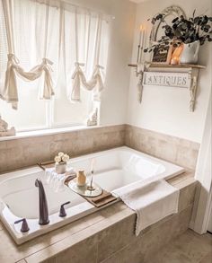 a bathtub with candles and flowers in the corner, next to a window filled with curtains