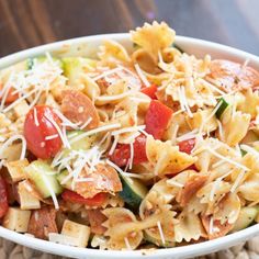 a pasta salad with tomatoes, zucchini and other toppings in a white bowl