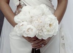 a woman in a wedding dress holding a bouquet of white peonies and roses