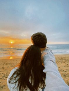 two people holding hands on the beach at sunset