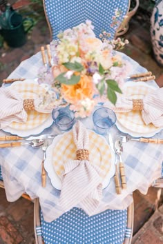 a blue and white table setting with gingham cloth napkins, flowers and plates