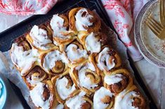 cinnamon rolls on a baking sheet with icing next to a cup of coffee and fork