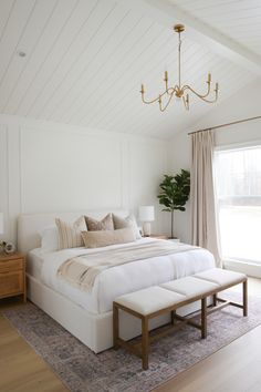 a large white bed sitting in a bedroom on top of a wooden floor next to a window