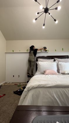 a woman standing on top of a bed next to a light fixture in a bedroom