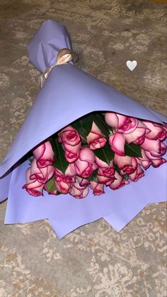 a bouquet of pink roses wrapped in purple paper on the floor next to a white heart