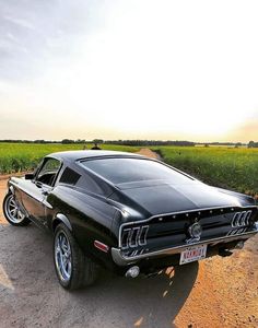 an old muscle car is parked on the side of the road in front of a corn field