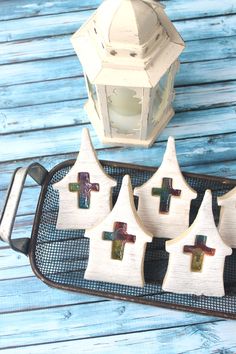 four wooden crosses are on a tray next to a lantern