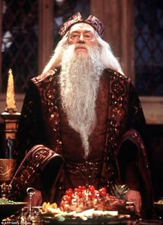 an old man with long white beard sitting in front of a table full of food