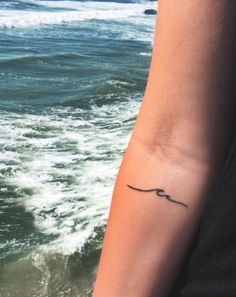 a woman's arm with a small tattoo on it, and the ocean in the background