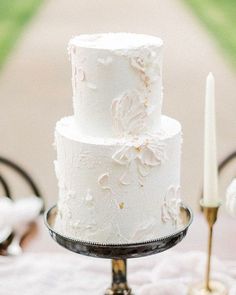 a three tiered white cake sitting on top of a table next to a candle