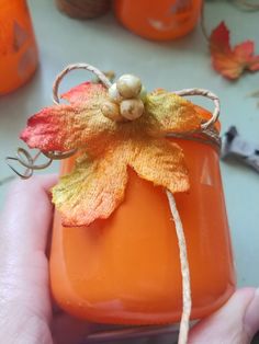 a person holding an orange jar with a flower on it's lid and string attached to the top