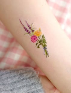 a woman's arm with flowers on it and a pink checkered blanket behind her