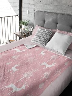 a bed with pink and white sheets, pillows and blankets on it in front of a brick wall