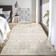 a bedroom with white walls and wooden flooring has a large rug on the floor