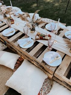 a table set up with plates and silverware on top of wooden pallets in the grass