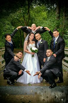 a bride and groom with their wedding party posing for a photo on a bridge in the woods