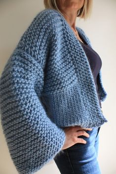 a woman is wearing a blue knitted cardigan and has her hands on her hips