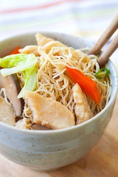 a bowl filled with noodles and vegetables on top of a wooden table