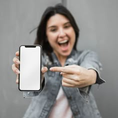 a woman pointing at her phone with an excited look on her face and holding it in one hand