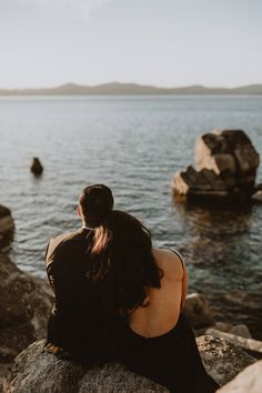 a woman sitting on top of a rock next to the ocean with her back turned