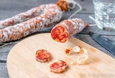 two sausages on a cutting board next to a glass of water