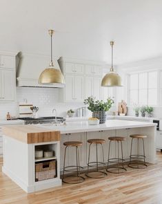 a kitchen with white cabinets and gold pendant lights hanging over the island in front of it