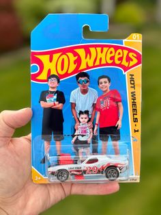 a hand holding up a toy car with three men on it's back and one man in the front