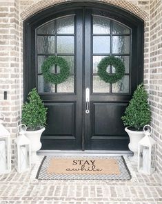 two potted plants on either side of the front door and an entrance mat that says stay awhile