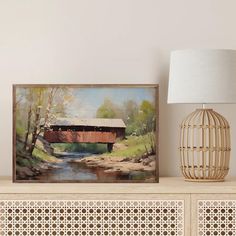 a painting on top of a dresser next to a lamp and a wooden cabinet with a basket