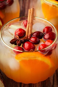 two glasses filled with drinks and garnished with orange slices, cinnamon sticks and cranberries