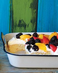 a cake in a pan with fruit on top and white frosting, sitting on a wooden table