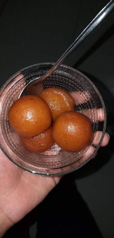 a hand holding a glass bowl filled with four brown balls and a spoon in it