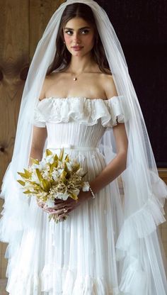 a woman in a white wedding dress holding a bridal bouquet and wearing a veil