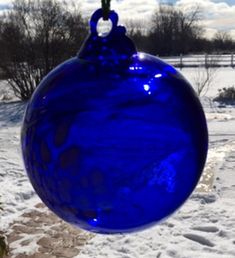 a blue glass ornament hanging from a tree in the snow on a sunny day