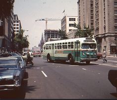 an old bus is driving down the street with other cars and people walking on the sidewalk