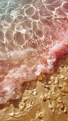 the sand is covered with pink and white foam as it sits next to the water