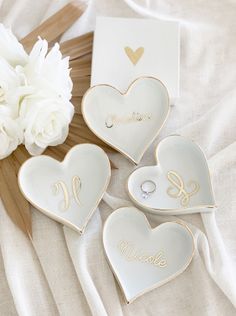 three heart shaped dishes sitting on top of a white blanket next to a bouquet of flowers