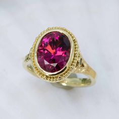 Exquisitely handcrafted in granulated 18KY gold, the “flower” of this one-of-a-kind ring is a 3.13ct rubellite tourmaline. Butterflies created in 18KW and each set with a 1.3mm VS/GH diamond are found on either side of the center gemstone. 2mm tsavorite garnets and the engraved leaf pattern create the flower’s stalk on the shank as engraved butterflies on the shank and beneath the center stone all flutter to the dazzling raspberry-red of the luscious rubellite tourmaline. Size 5.5, but each ring Yellow Gold Ruby Ring With Tourmaline Center Stone, Rubellite Tourmaline, Raspberry Red, Tsavorite Garnet, Special Ring, Butterfly Ring, The Butterfly, Leaf Pattern, Tourmaline