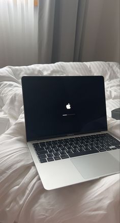 an apple laptop computer sitting on top of a white bed covered in sheets and pillows