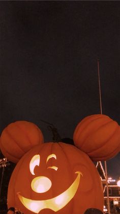 a mickey mouse pumpkin carved into the shape of a face at night with people looking on