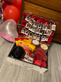 an open suitcase filled with lots of items on top of a wooden floor next to balloons