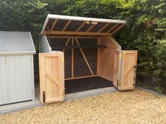 two storage sheds with doors open in the middle of a gravel lot next to trees