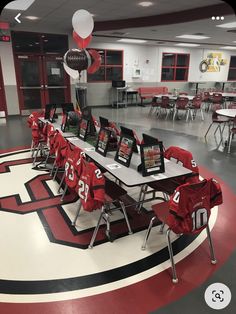 a room filled with lots of tables and chairs covered in red cloths next to soccer balls